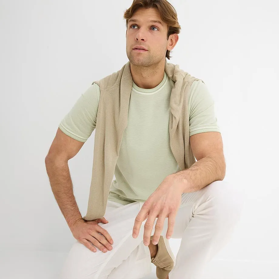 Maglietta chiara con un maglione leggero e pantaloni bianchi.