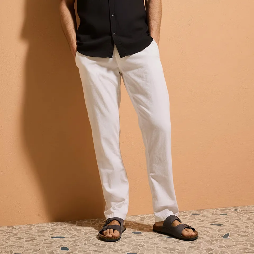 Un contrasto elegante: una camicia nera abbinata a pantaloni bianchi e leggeri. Dei sandali casual completano il look.
