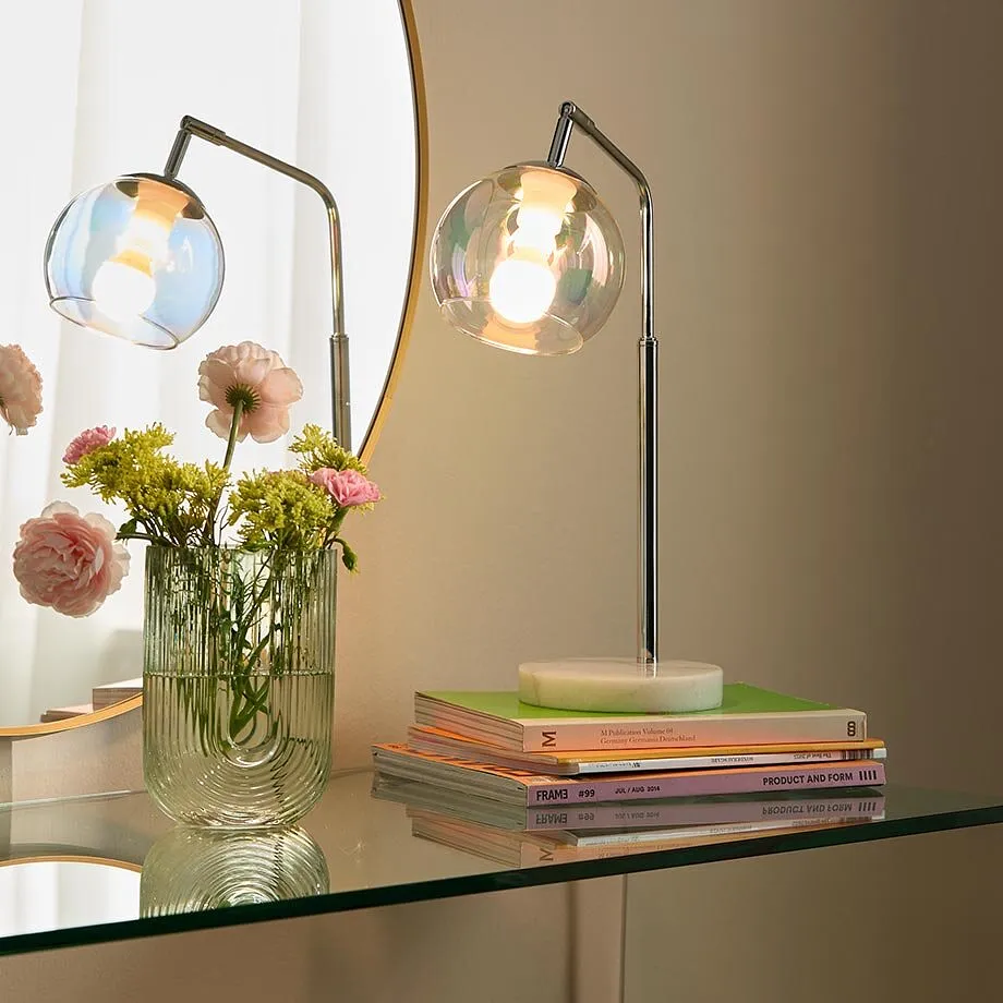 Un'elegante lampada da tavolo con paralume in vetro illumina con stile la zona giorno moderna con tonalit&agrave; calde.