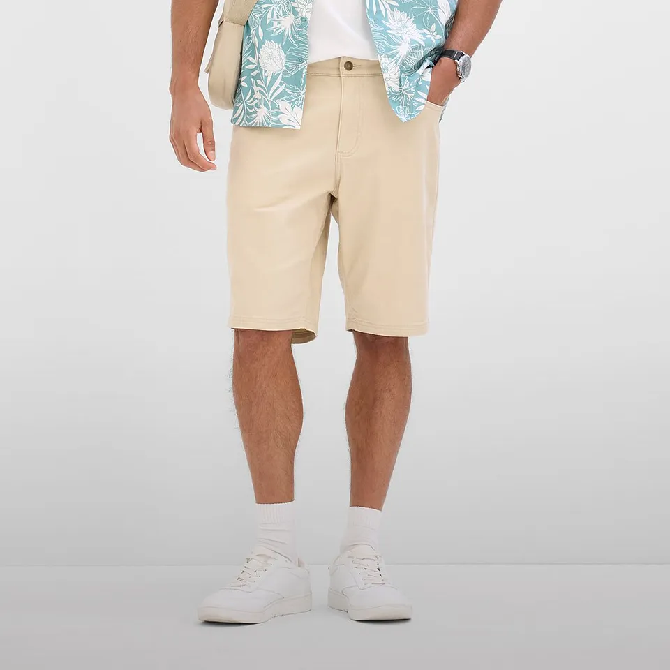 Un outfit estivo casual con bermuda beige, camicia a fantasia e sneakers bianche.