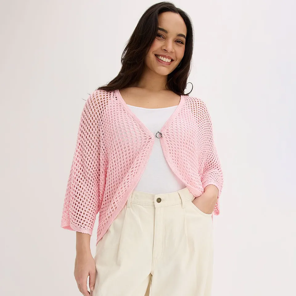 Una donna indossa un cardigan rosa sopra un top bianco e pantaloni color crema.