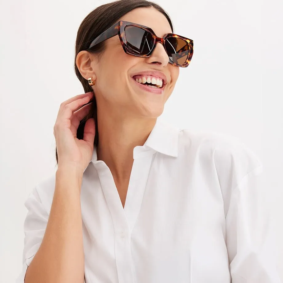 Una donna indossa una camicetta bianca e occhiali da sole alla moda.