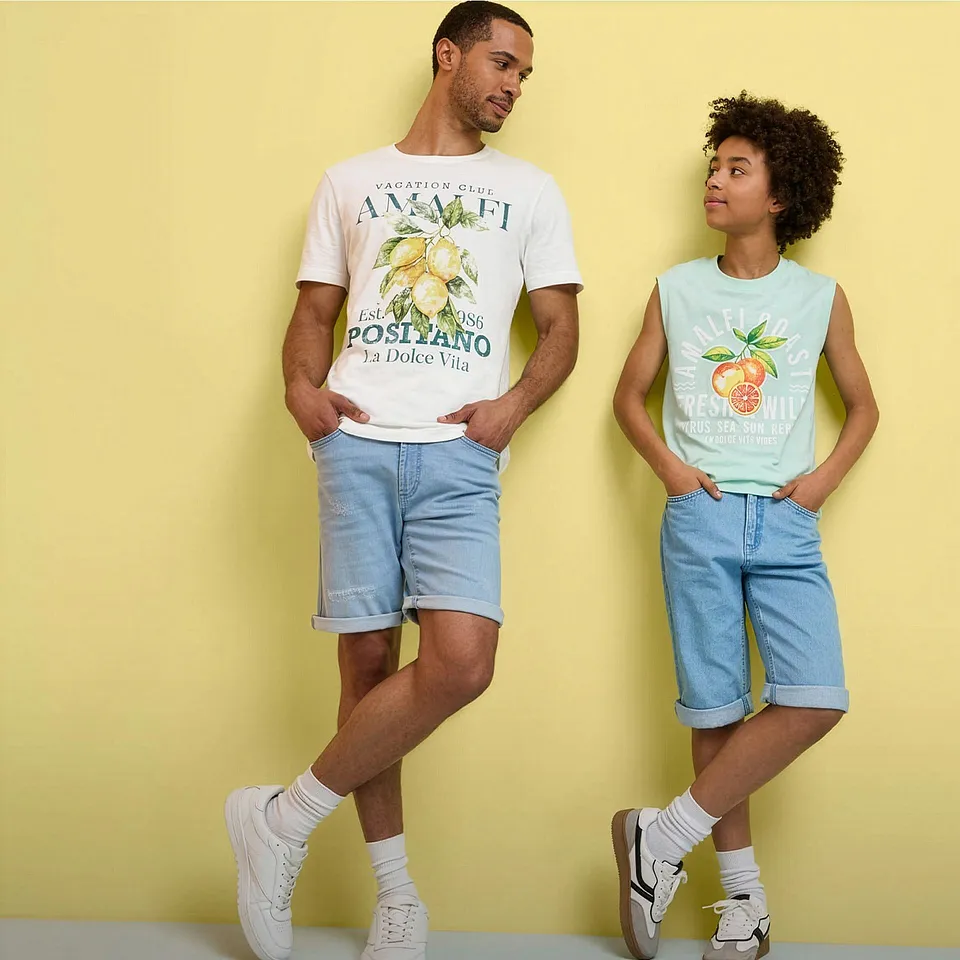 Due persone indossano abbigliamento estivo con magliette stampate, pantaloncini di jeans e scarpe da ginnastica bianche.