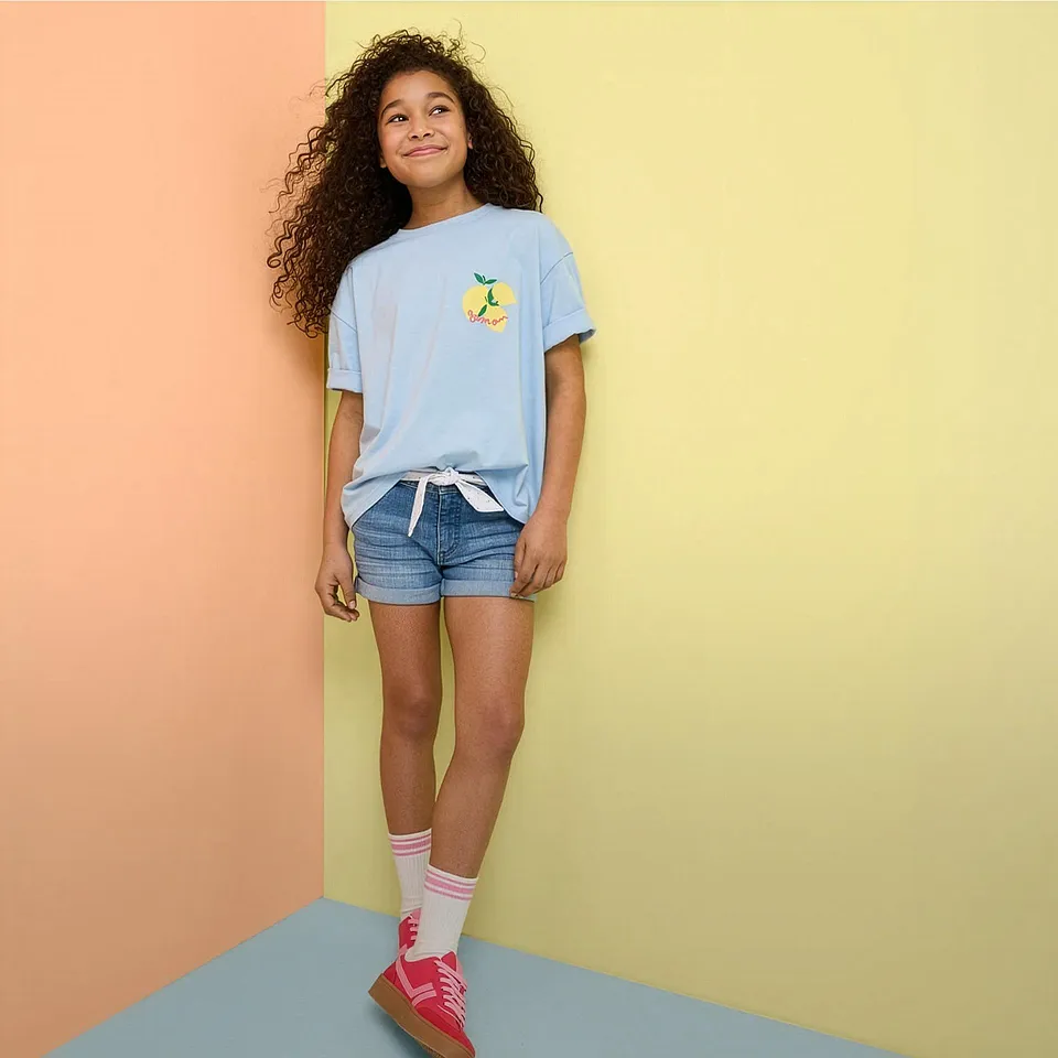 Outfit estivo con maglietta azzurra, shorts di jeans e sneaker colorate.