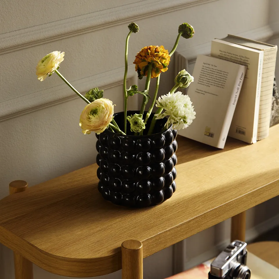 Vaso nero con fiori freschi su un tavolo di legno accanto a dei libri, disposti in modo decorativo.