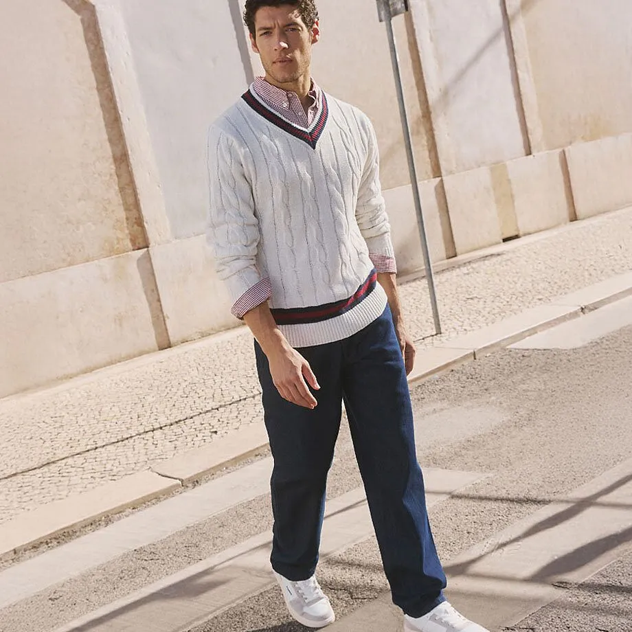 Maglione bianco con motivo a treccia sopra una camicia, pantaloni scuri e scarpe da ginnastica bianche.