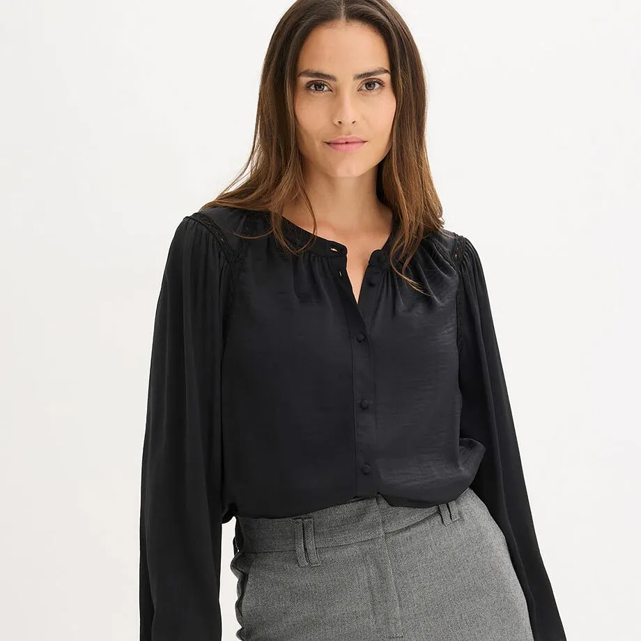 Elegante camicetta nera con scollo a V, abbinata a pantaloni grigi.