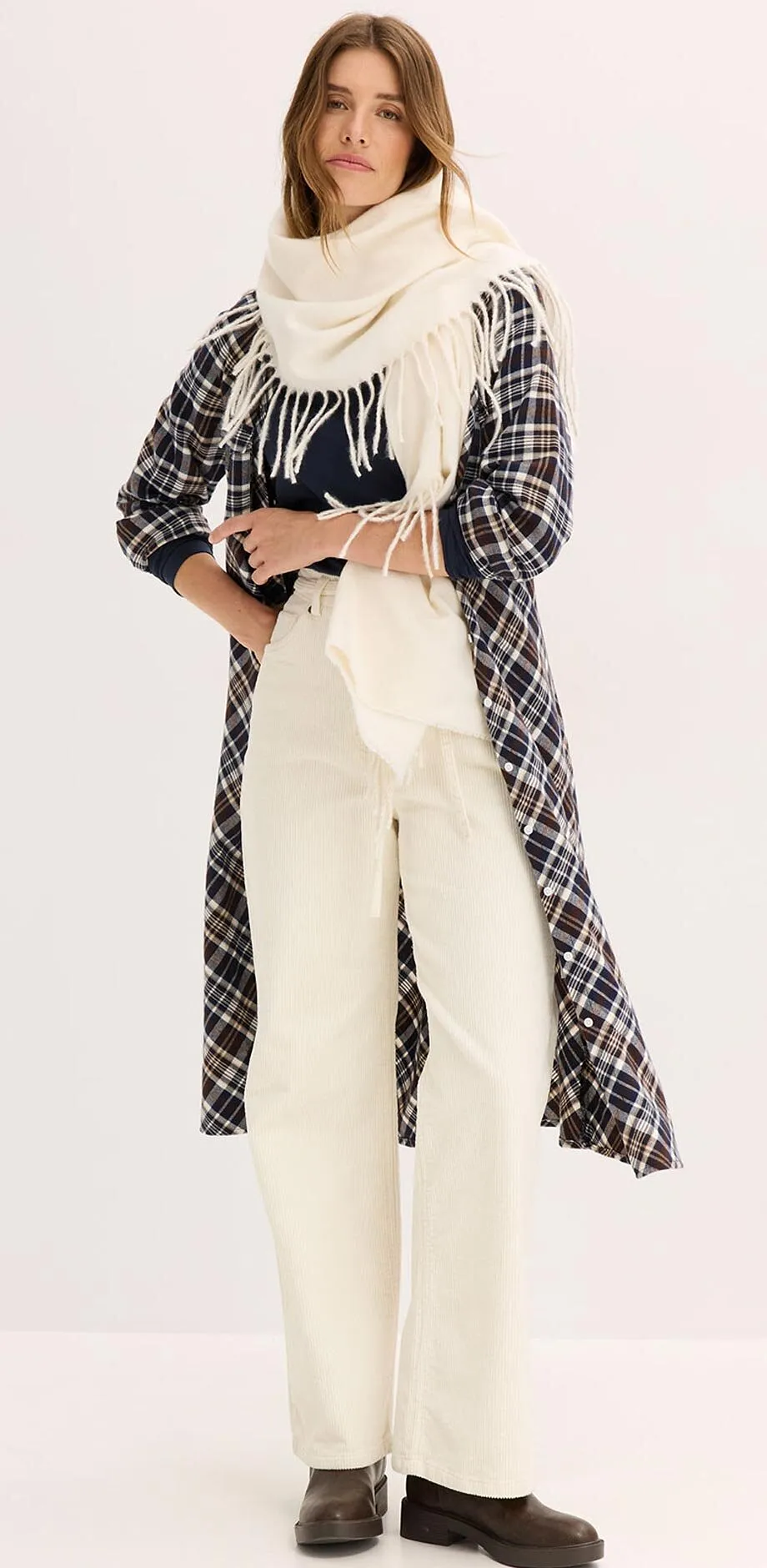 Cappotto a quadri su outfit color crema con maglione a collo alto, sciarpa larga e pantaloni.