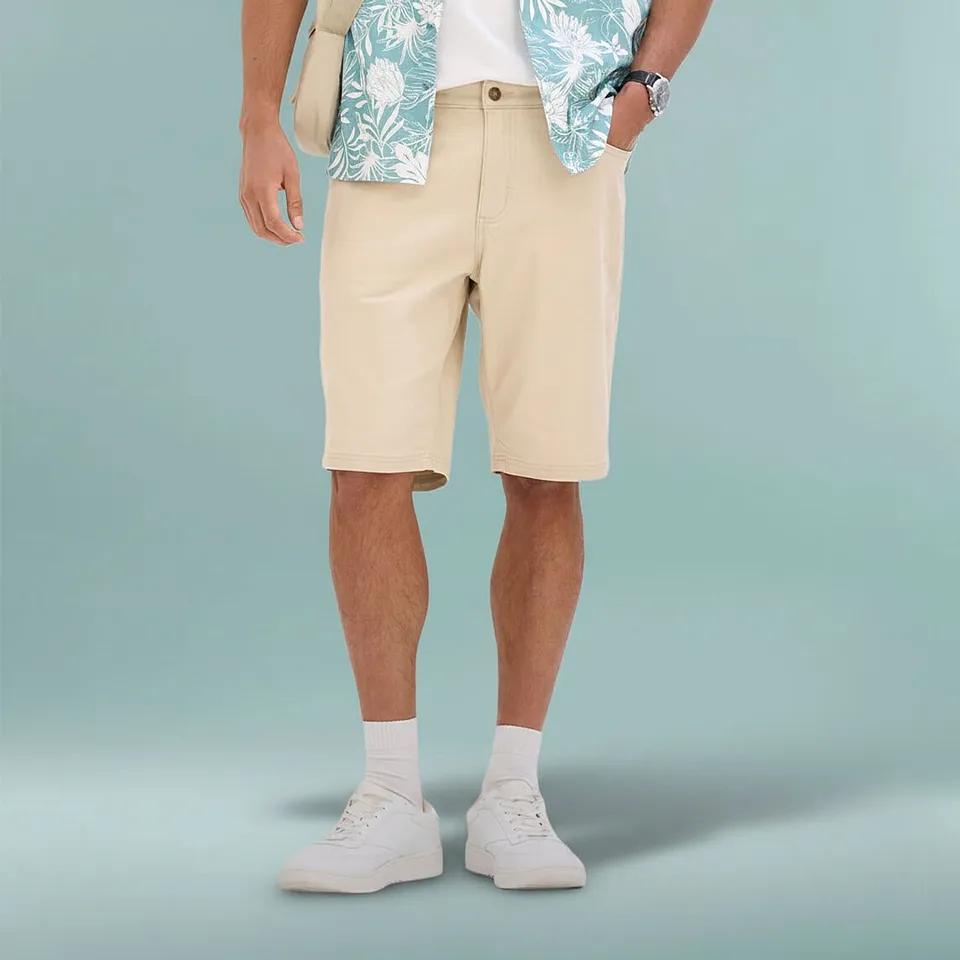 Un outfit estivo casual con bermuda beige, camicia a fantasia e sneakers bianche.