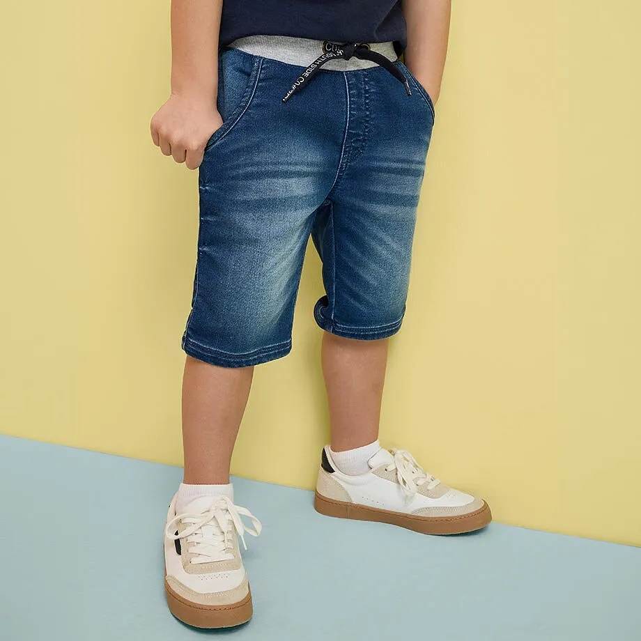 Un bambino indossa pantaloncini di jeans blu e scarpe da ginnastica bianche.