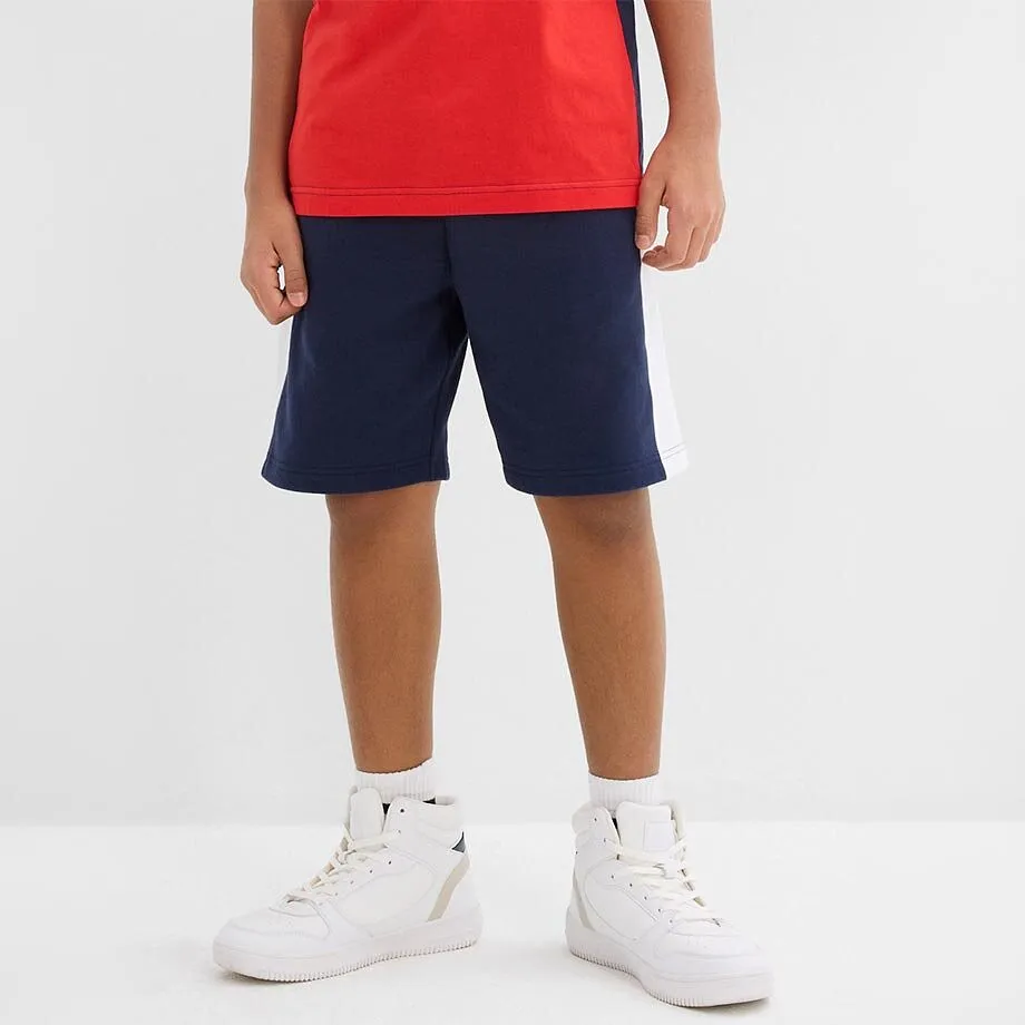Un bambino indossa una maglietta rossa e pantaloncini blu scuro.