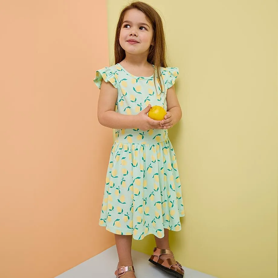 Una bambina indossa un vestito turchese e dei sandali.