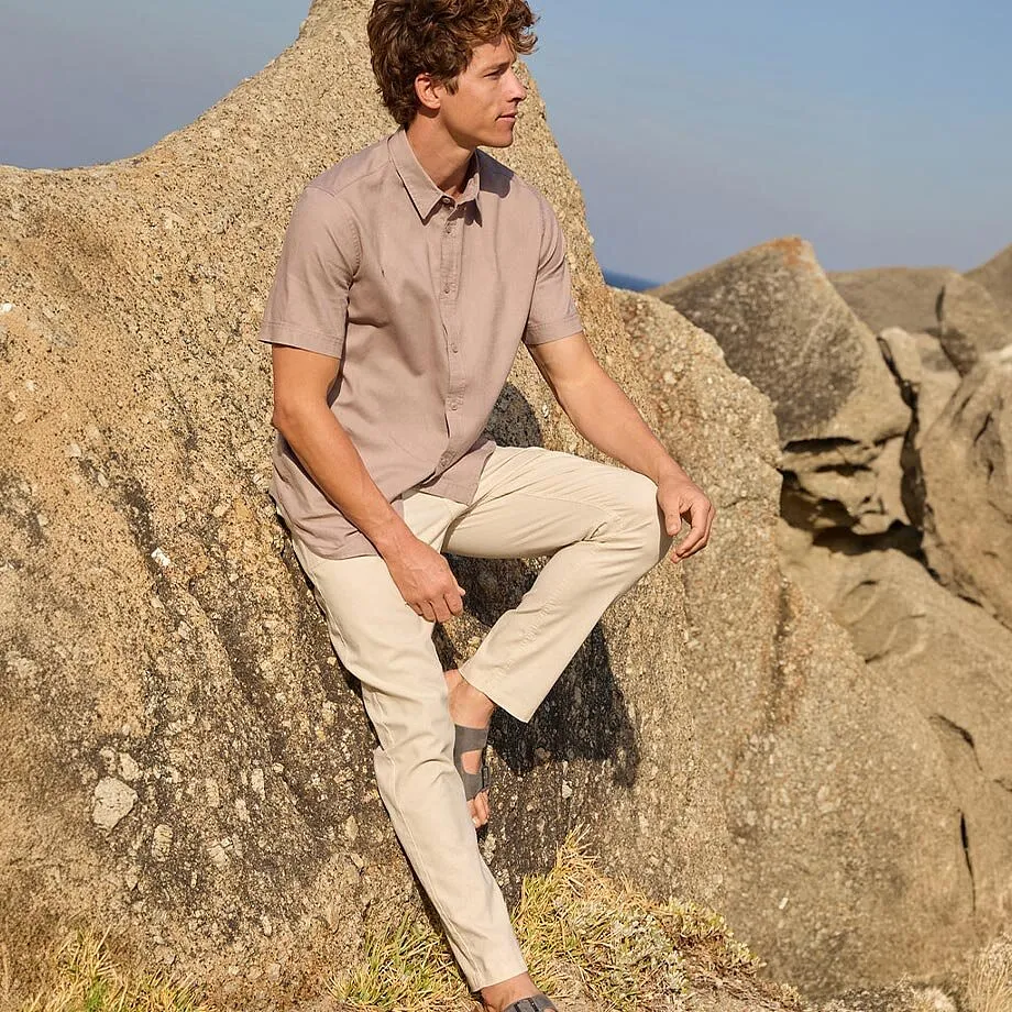 Un uomo indossa una camicia beige e pantaloni chino chiari con dei sandali sulla spiaggia.