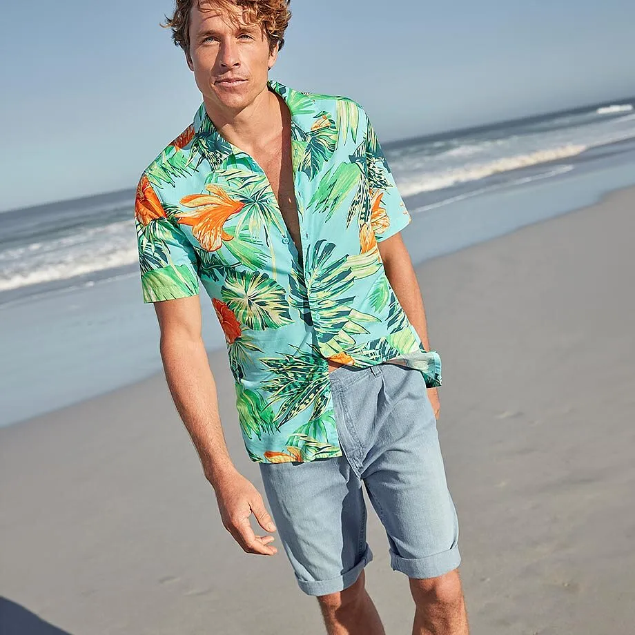 Un uomo indossa una camicia hawaiana colorata e pantaloncini chiari sulla spiaggia.