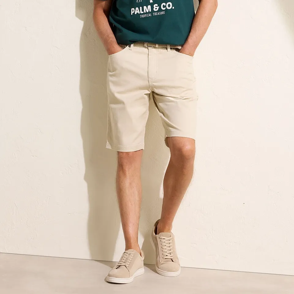 Maglietta verde con stampa, bermuda chino beige e scarpe da ginnastica chiare.