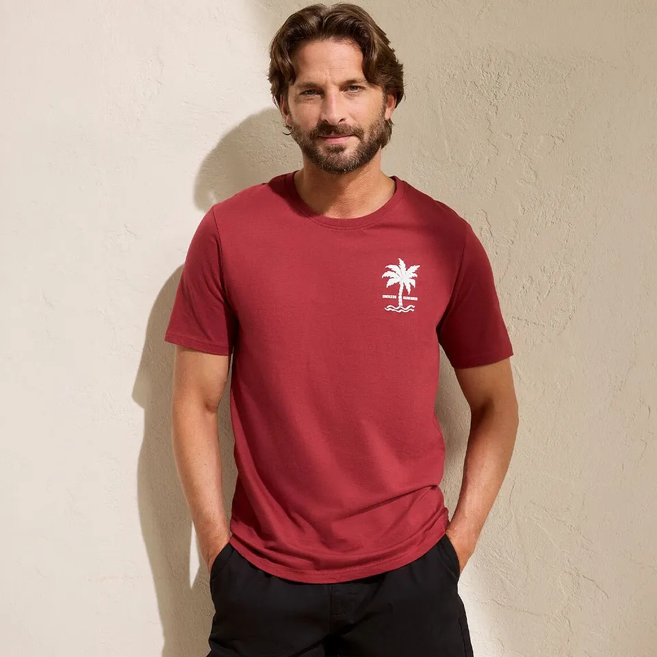 Un uomo indossa una maglietta rossa con un piccolo logo bianco e pantaloni neri.