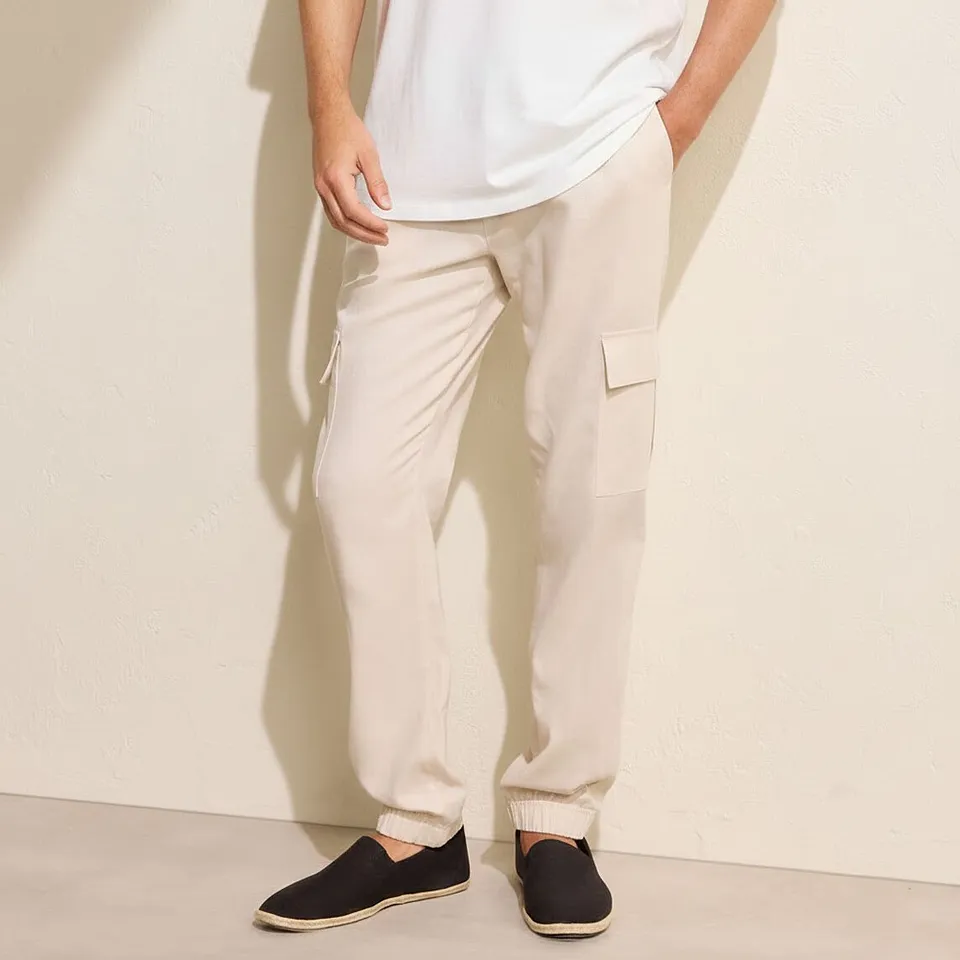 Un look casual con maglietta bianca, pantaloni cargo beige e scarpe slip-on scure.