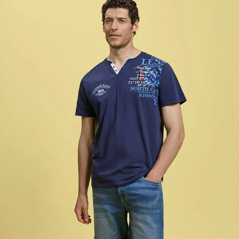 Un uomo indossa una maglietta serafino blu scuro dal taglio casual con una stampa accattivante e dei jeans chiari.