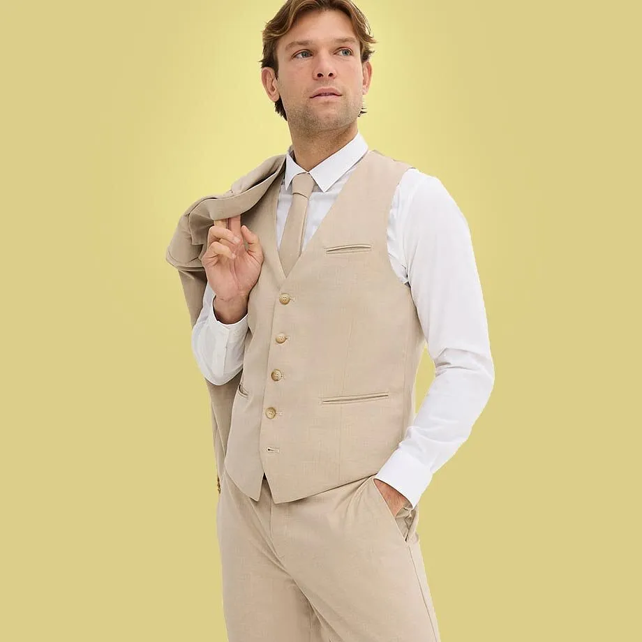 Un uomo indossa un completo beige con camicia bianca e gilet abbinato.