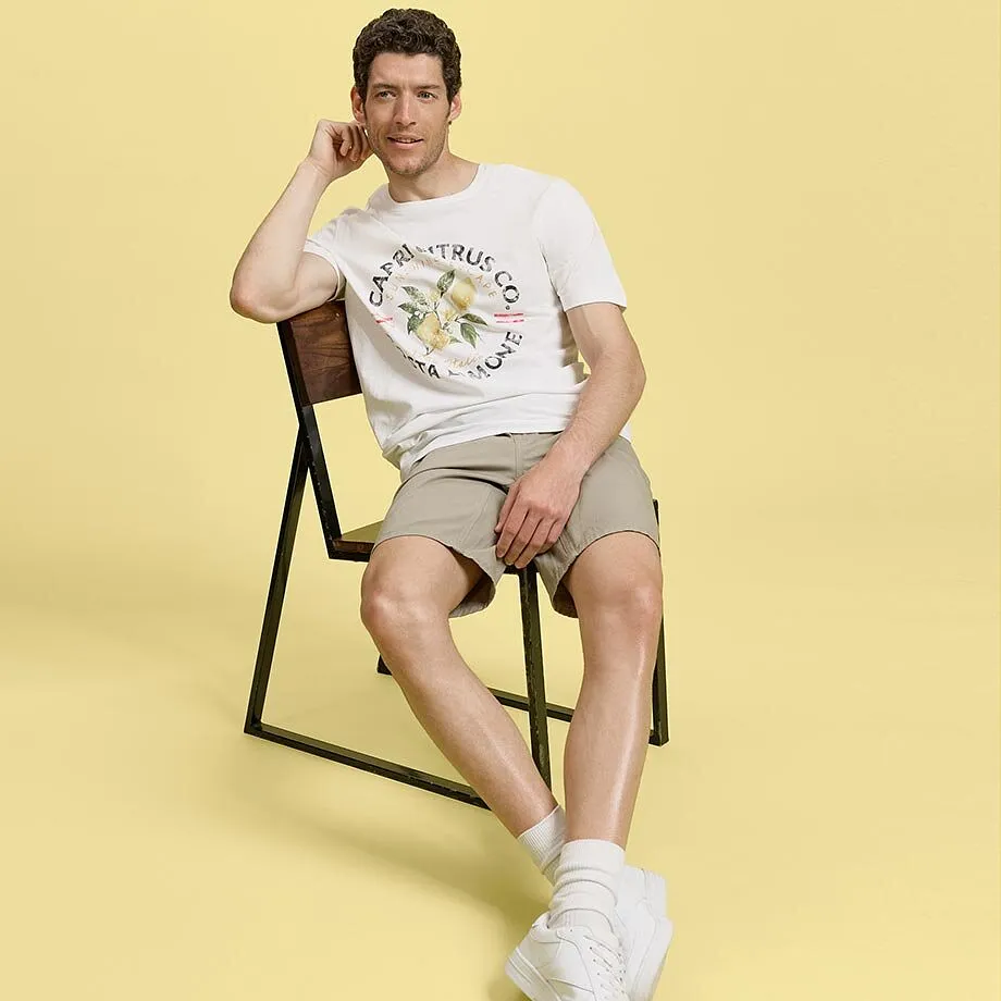Un outfit estivo comodo: maglietta bianca, pantaloncini beige e scarpe da ginnastica bianche.