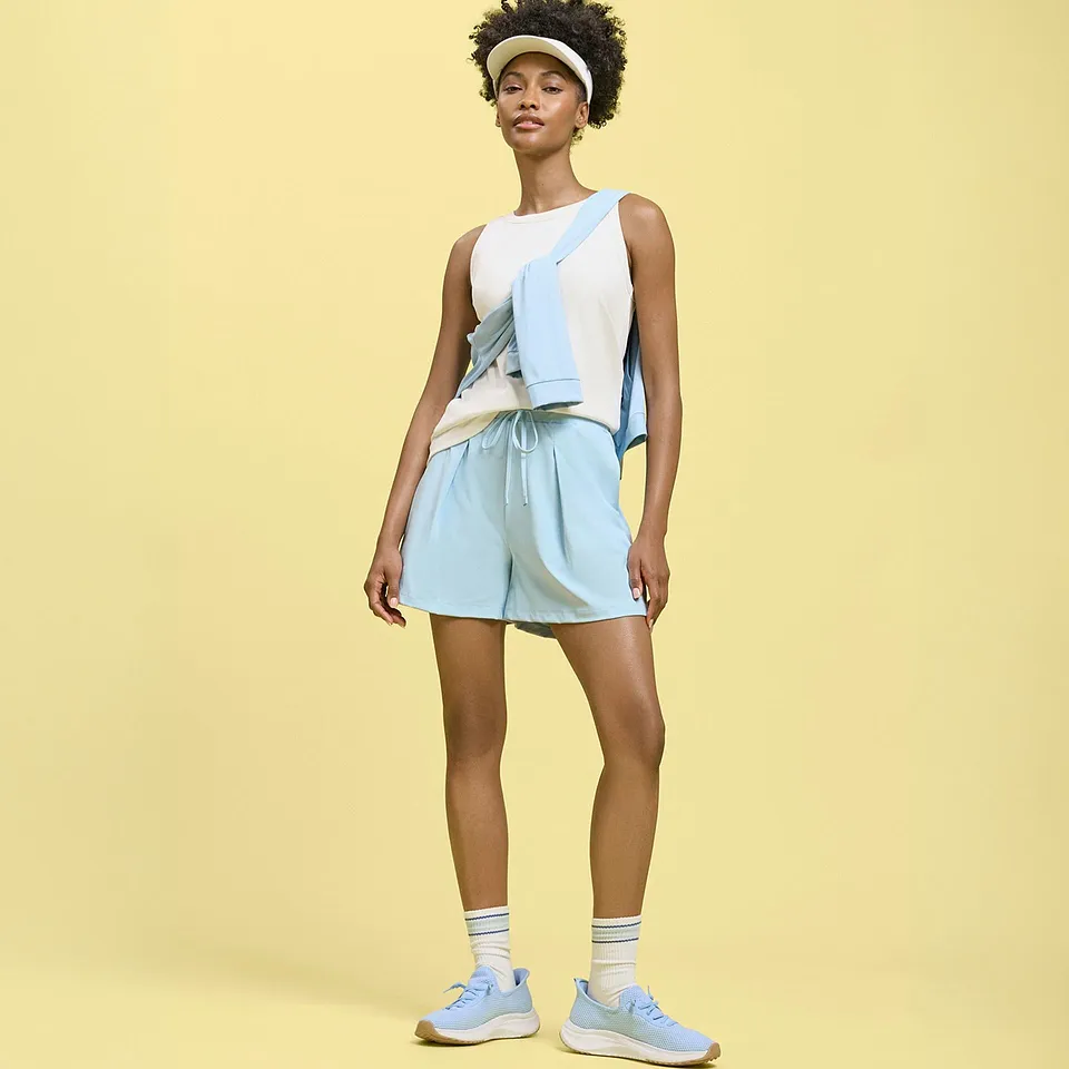 Top bianco, pantaloncini azzurri e maglione, con scarpe da ginnastica e berretto.