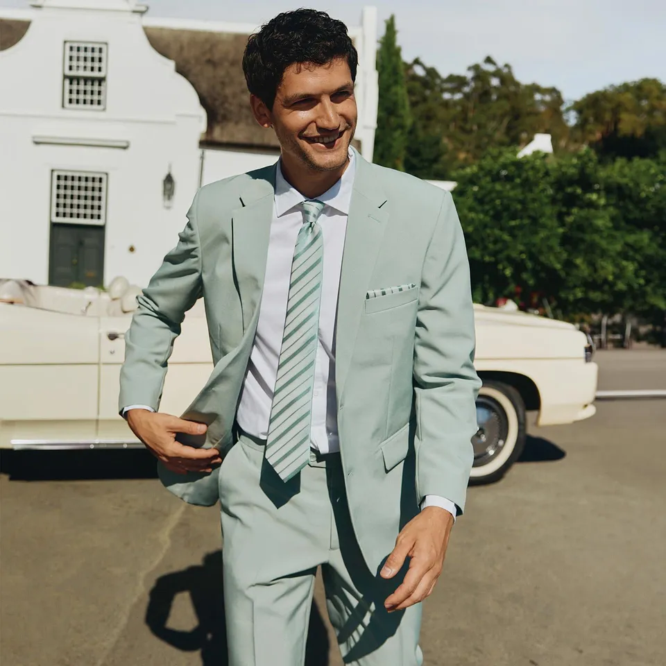 Un signore elegante con un abito verde chiaro, una camicia bianca e una cravatta a righe abbinata.