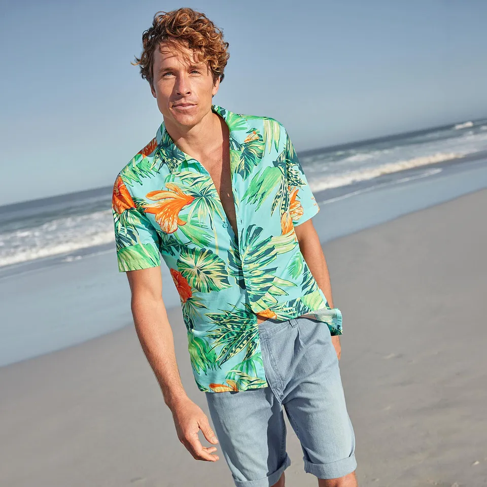 Un uomo indossa una camicia hawaiana colorata e pantaloncini chiari sulla spiaggia.