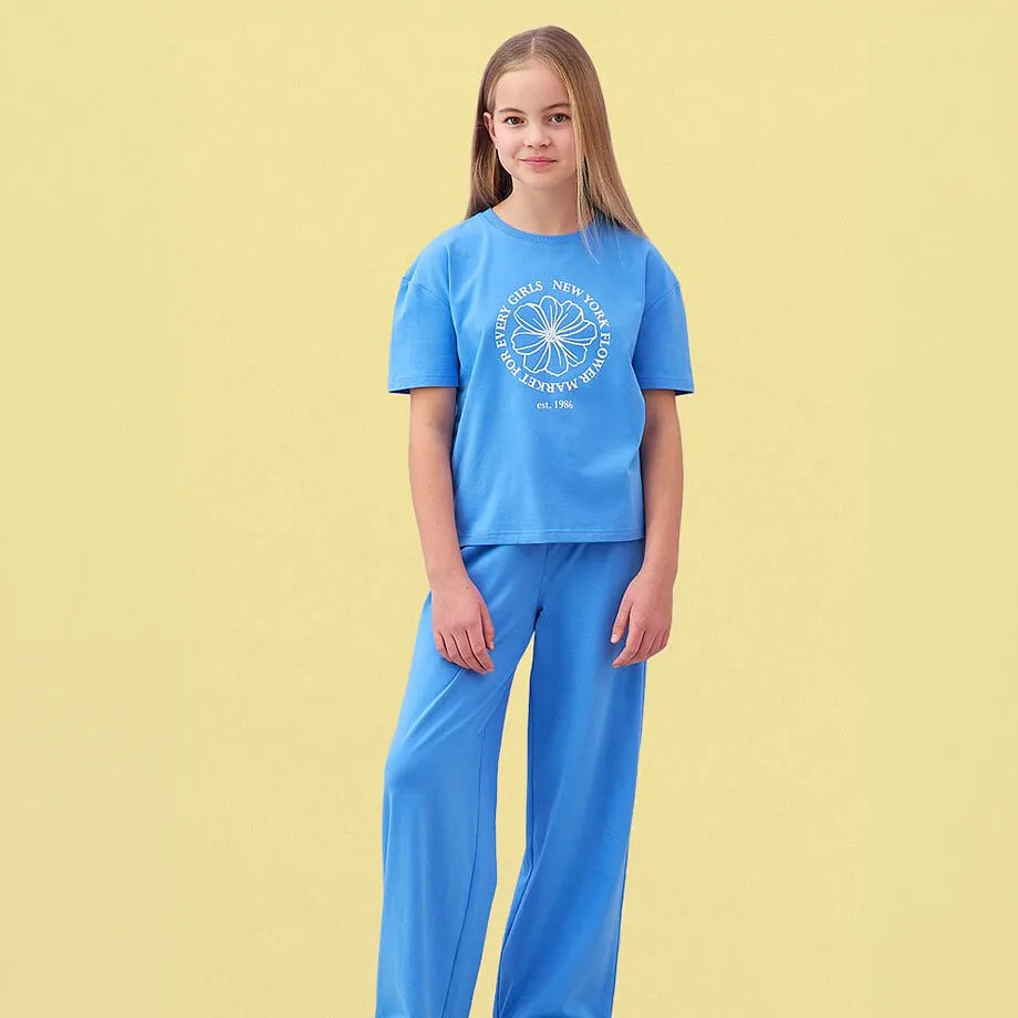Una maglietta azzurra con una stampa e pantaloni larghi blu abbinati.