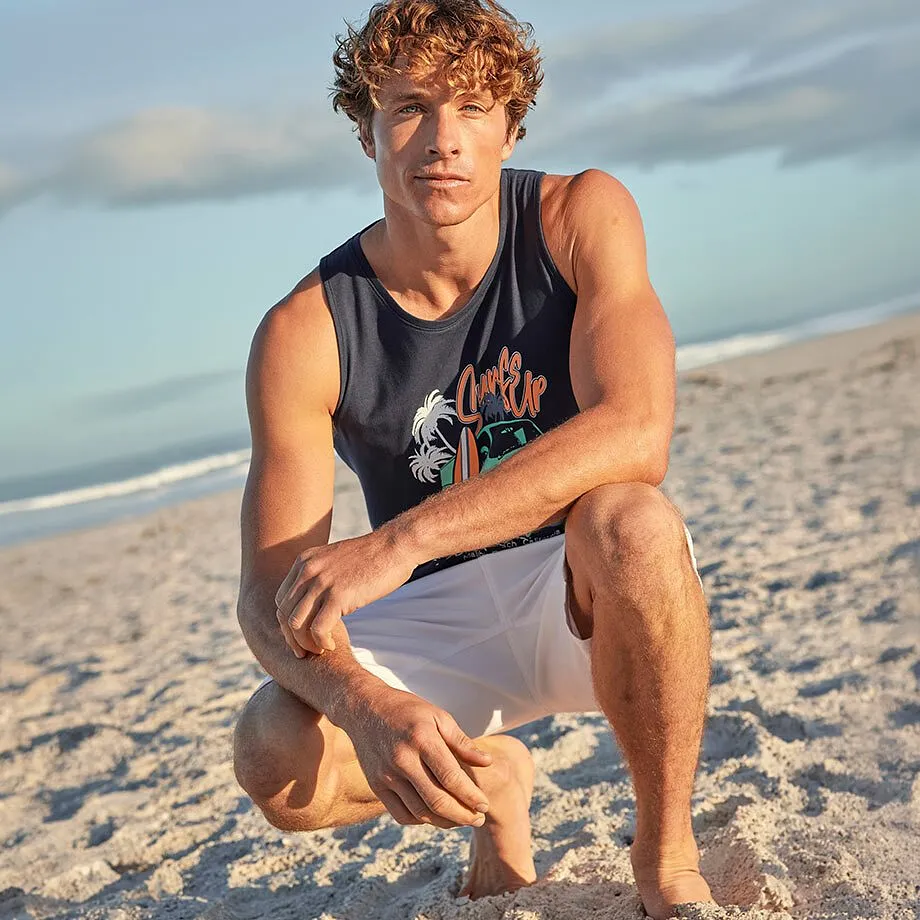 Un uomo indossa una canottiera blu con una stampa e dei pantaloncini bianchi in spiaggia.