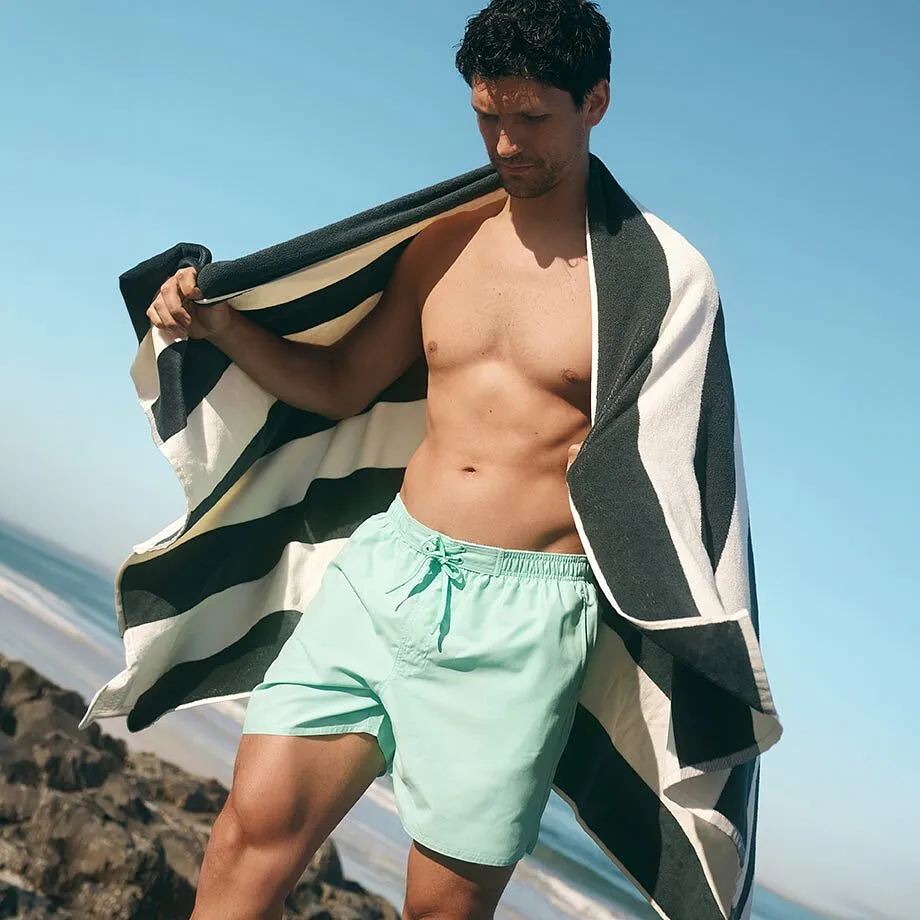 Un uomo indossa un paio di pantaloncini da bagno verde menta e ha un asciugamano a righe sulle spalle.
