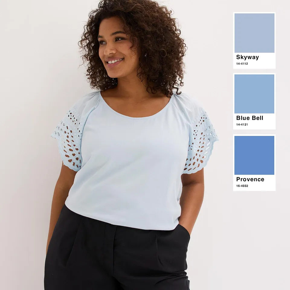 Maglietta fresca color azzurro con maniche traforate, abbinata a pantaloni semplici di colore scuro.