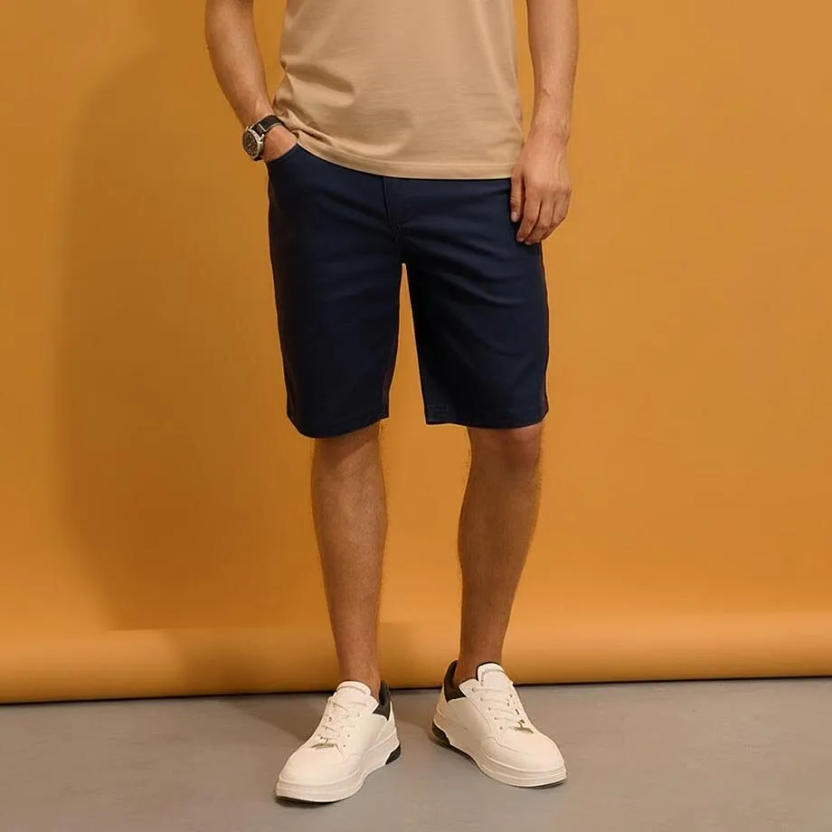Maglietta beige, pantaloncini blu scuro e sneaker bianche.