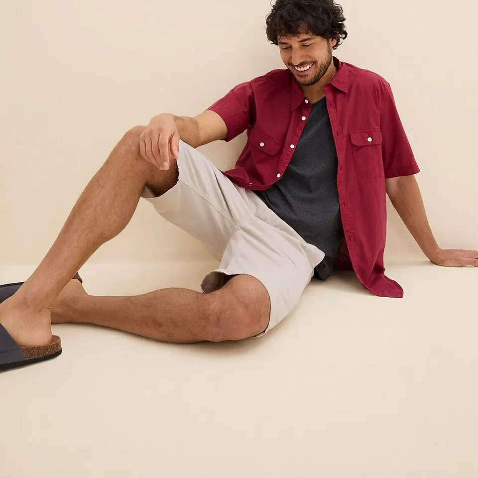 Camicia rossa a maniche corte con maglietta scura sotto, pantaloncini chiari e sandali comodi.