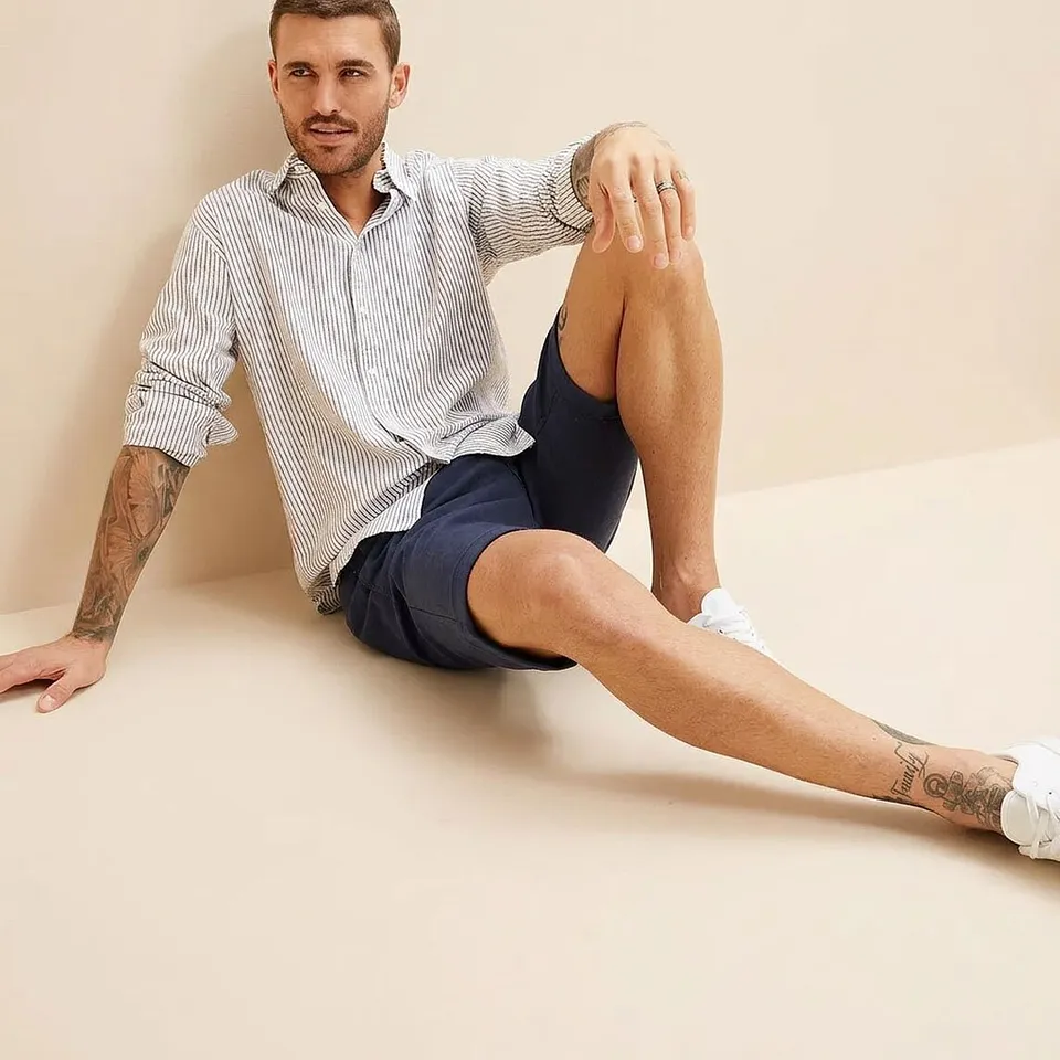 Outfit perfetto con camicia a righe, pantaloncini blu scuro e sneaker bianche.