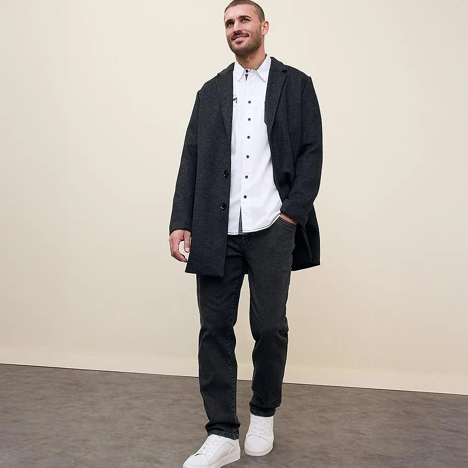 Cappotto scuro su camicia bianca, jeans abbinati e scarpe da ginnastica bianche.