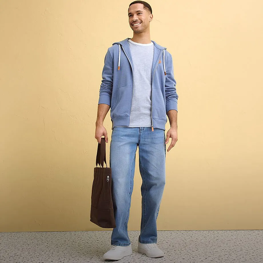 Una felpa blu con cappuccio, una maglietta chiara, dei jeans e delle sneakers bianche creano uno stile disinvolto.