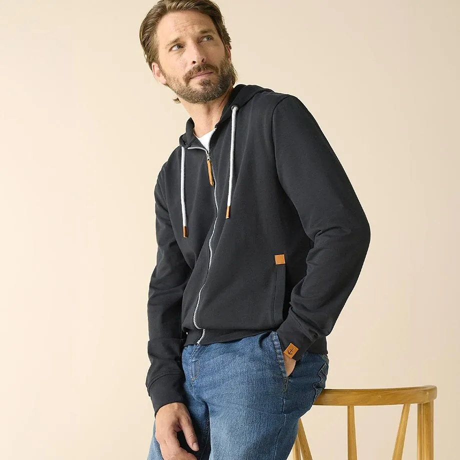 Giacca felpata scura con cerniera, jeans azzurri, maglietta bianca.