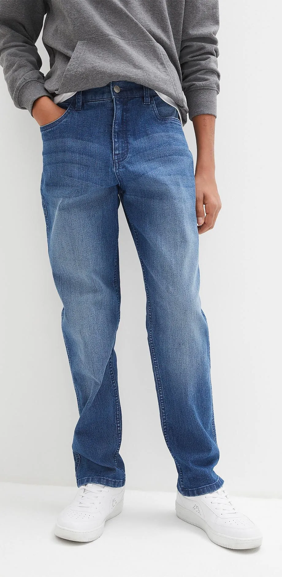 Una felpa grigia, jeans blu e sneaker bianche creano un look casual.