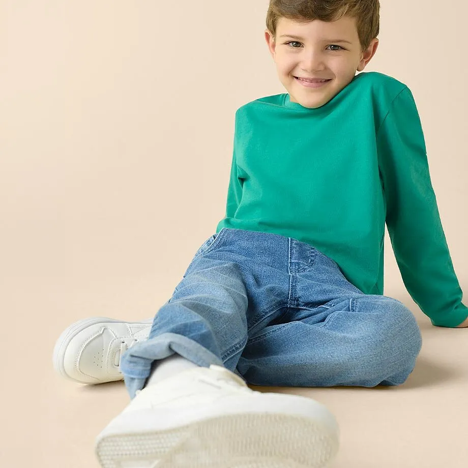 Maglia verde a maniche lunghe, jeans blu e sneaker bianche: un outfit comodo per i bambini.