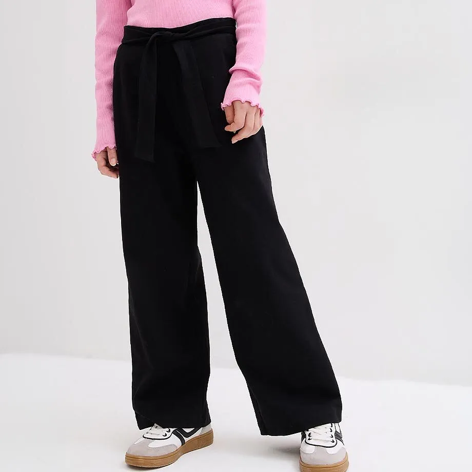 Maglia rosa, pantaloni larghi neri con laccio e sneaker sportive.