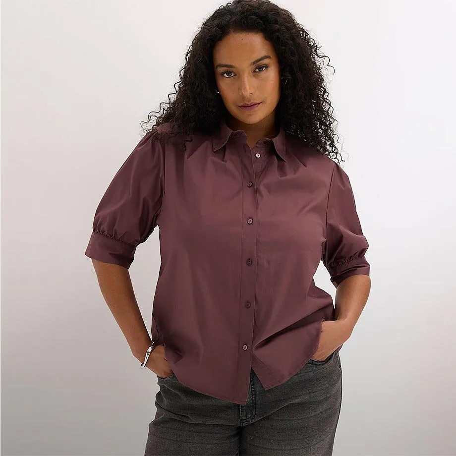 Camicetta color bordeaux con eleganti maniche a sbuffo e colletto, abbinata a jeans scuri.
