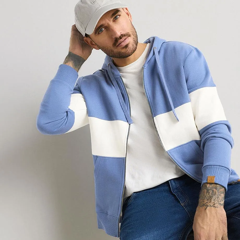 Look casual: felpa blu con cappuccio, maglietta bianca, jeans e berretto grigio.