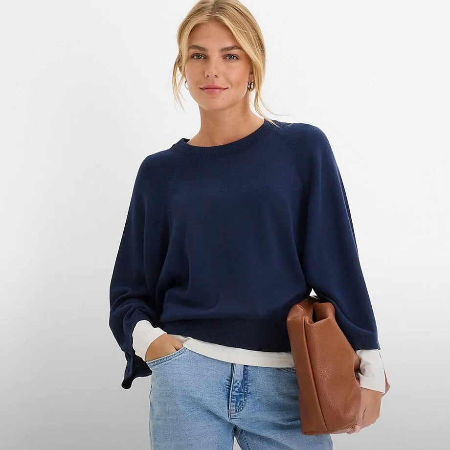 Maglione blu scuro, jeans chiari e una borsa marrone.