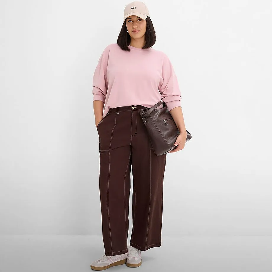 Felpa rosa, pantaloni larghi marroni con cuciture, berretto beige e borsa scura.