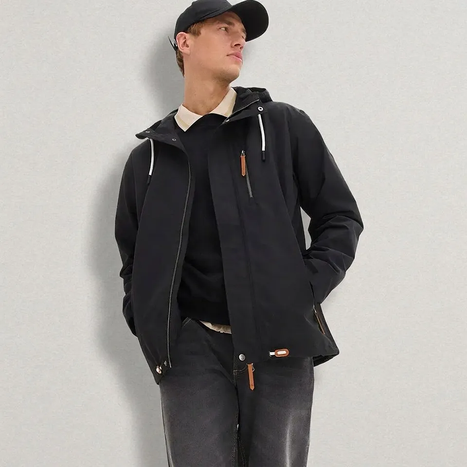 Giacca nera con cappuccio, jeans, maglione e berretto.