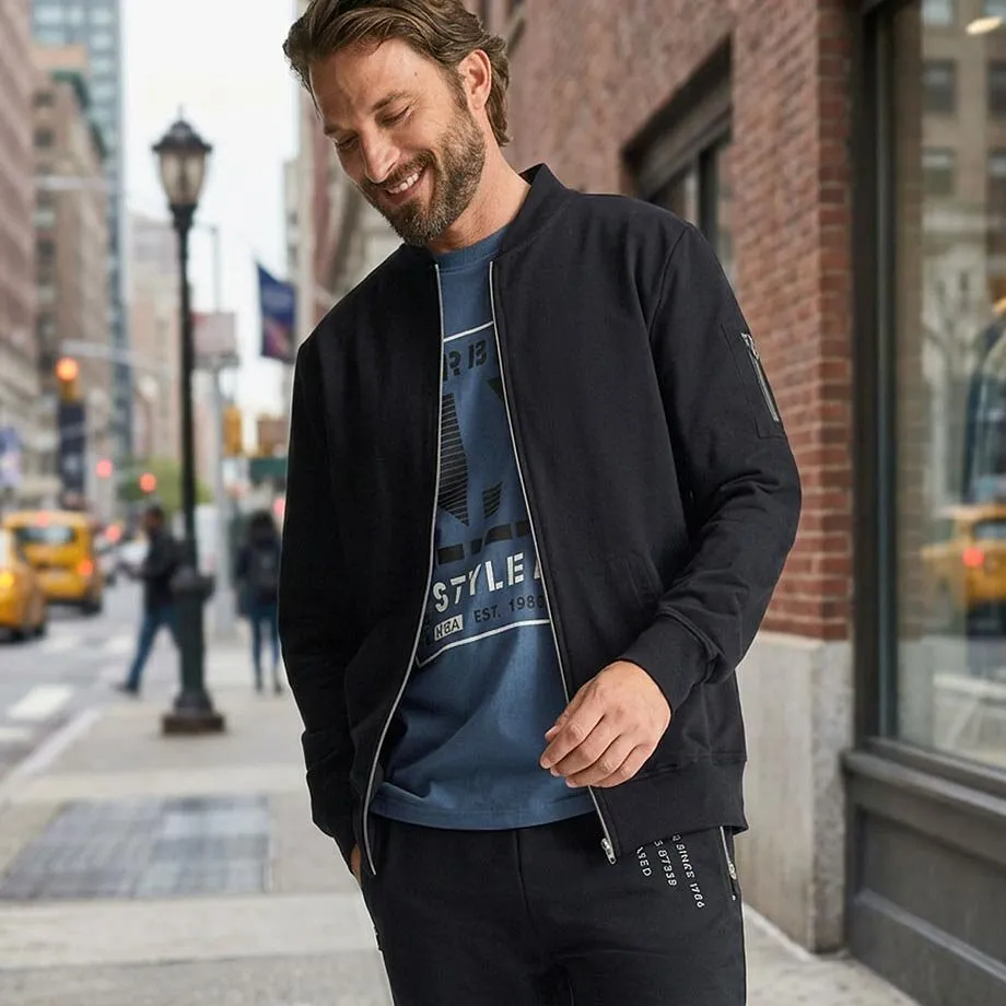 Giacca bomber nera, maglietta blu, pantaloni scuri e scarpe da ginnastica bianche.