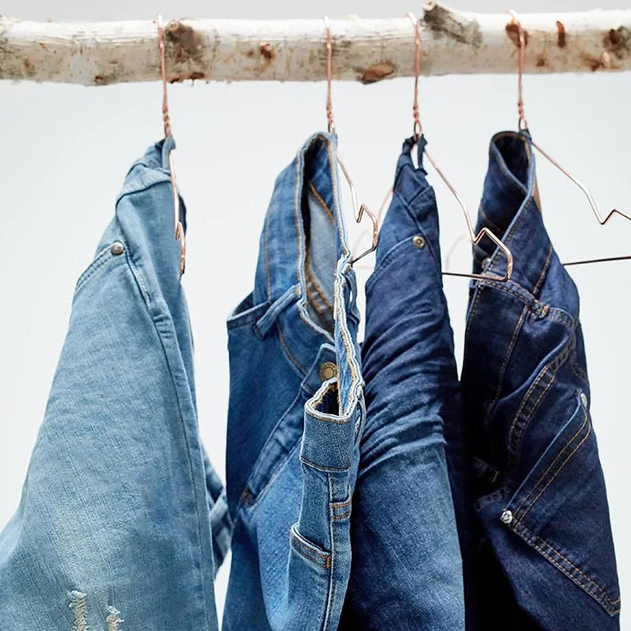 Una serie di jeans blu con diversi effetti di lavaggio &egrave; appesa ordinatamente alle grucce.