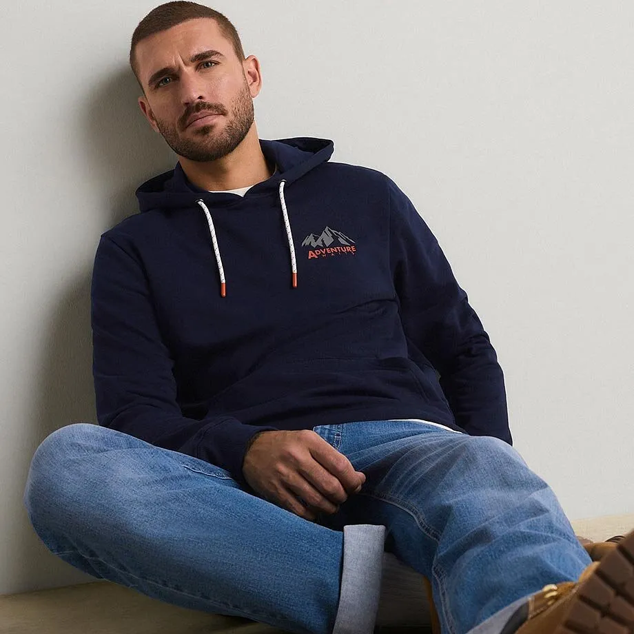 Felpa con cappuccio blu scuro con un motivo di montagna e un paio di jeans blu dal look casual.