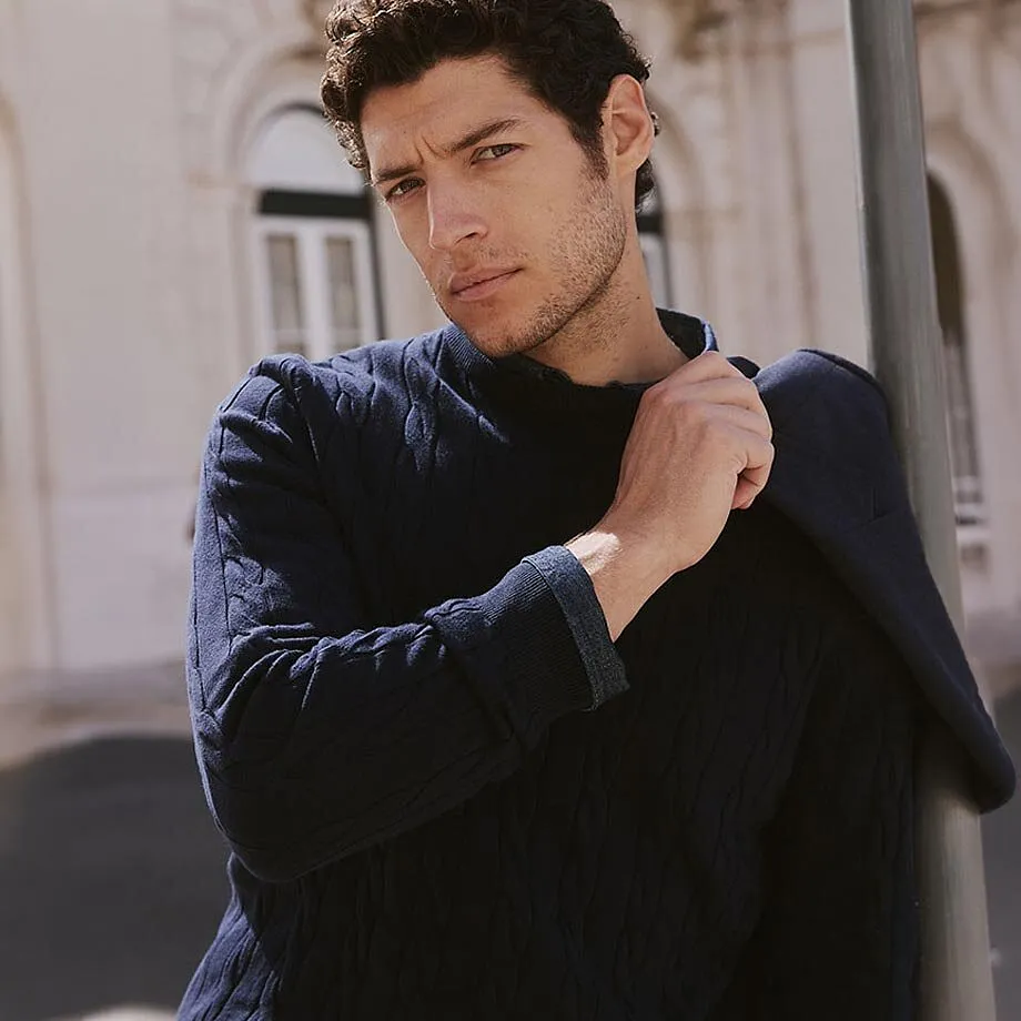 Un maglione blu scuro a trama ruvida e una giacca indossata con disinvoltura sulle spalle.