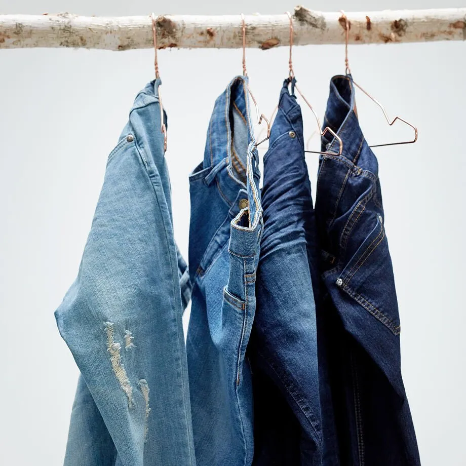 Jeans in diverse tonalit&agrave; di blu sono appesi a delle grucce su un ramo di legno.